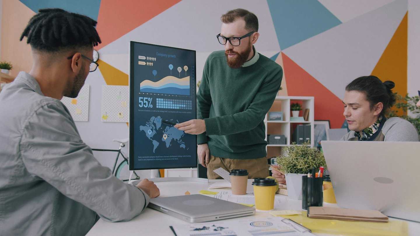 Três pessoas conversando diante de um monitor com gráficos