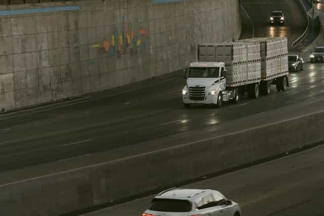 Caminhão carregando contêineres brancos em uma rodovia