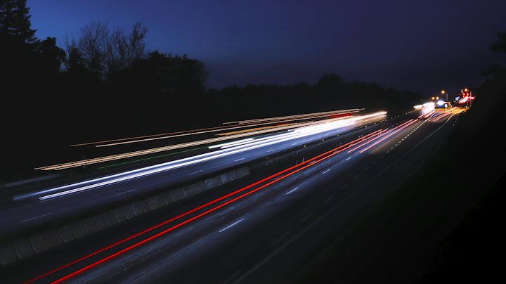Rodovia à noite em longa exposição, com rastros de luz dos carros